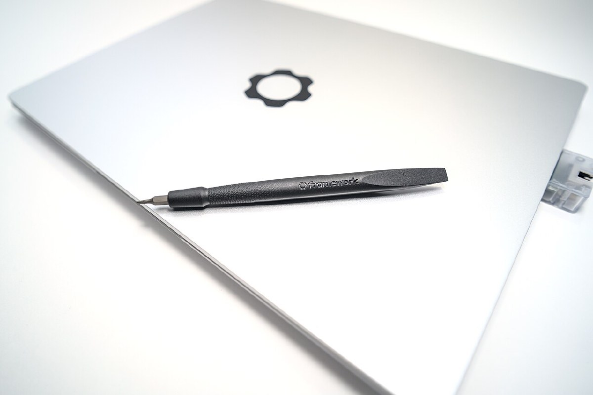 Framework Laptop 13 closed, with the included combination screwdriver-spudger tool resting on the lid and an expansion card partially ejected