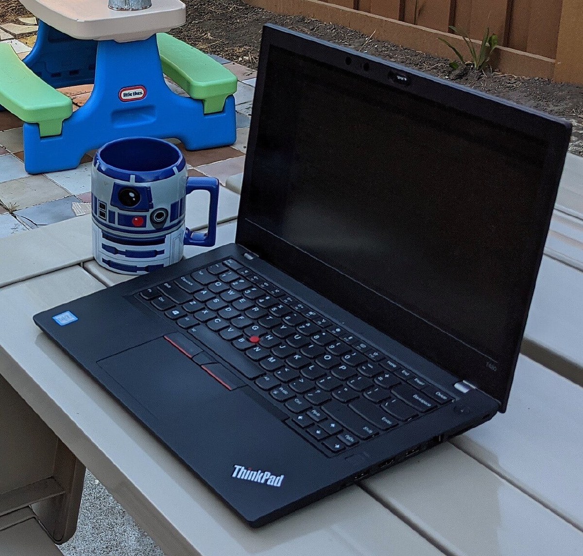 Lenovo ThinkPad T480 open on an outdoor table, showing the black chassis, keyboard with red TrackPoint, and ThinkPad logo