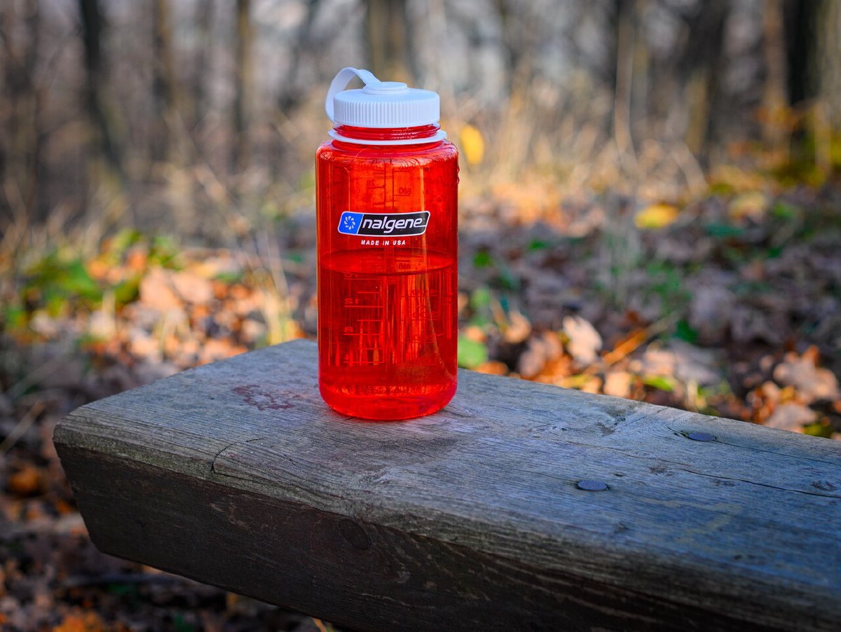 Red Nalgene 32 oz Wide Mouth bottle with white loop-top lid standing on a wooden bench outdoors