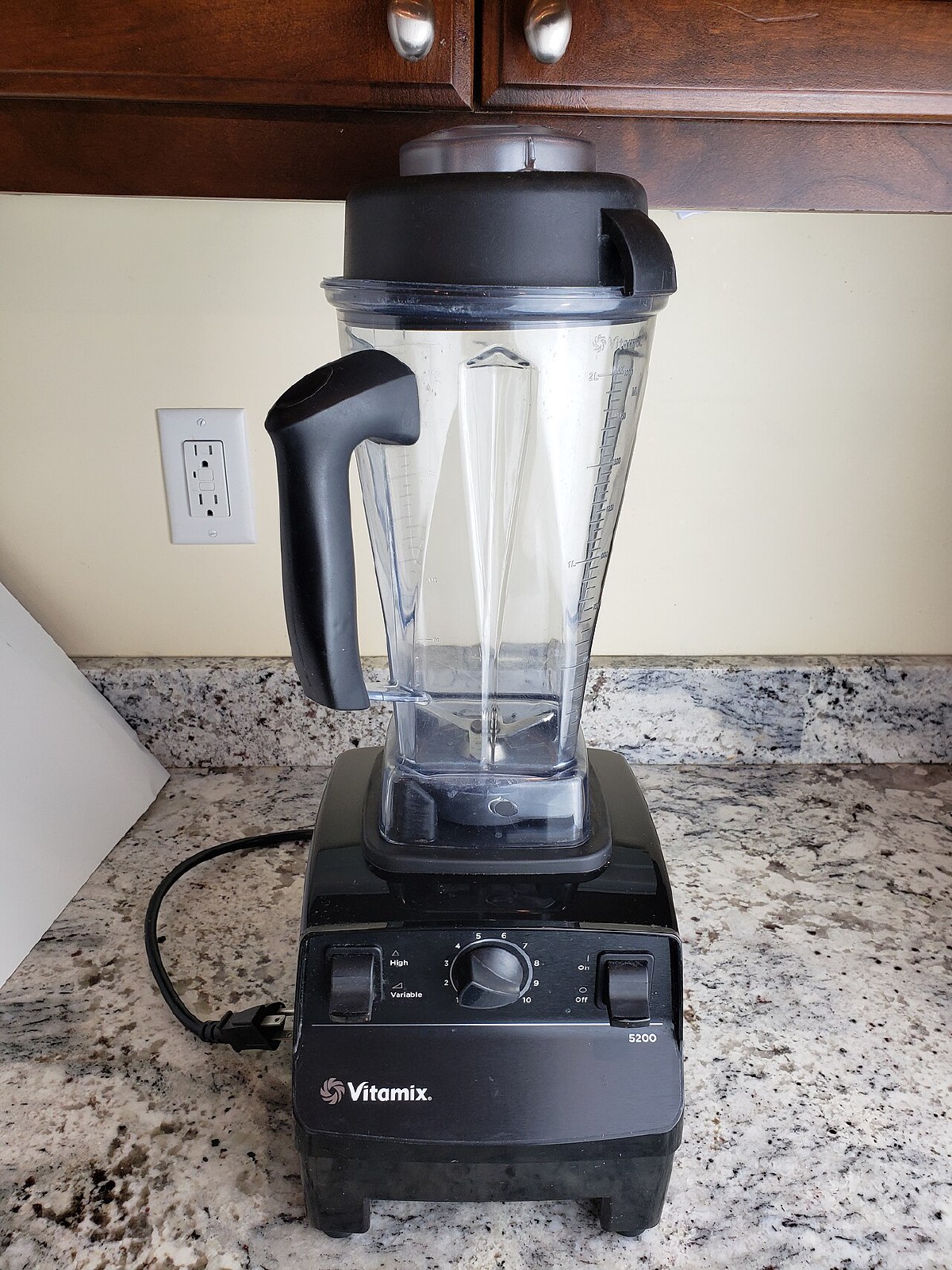 Black Vitamix 5200 blender with clear 64-ounce container on a granite kitchen counter, variable-speed dial visible on the base