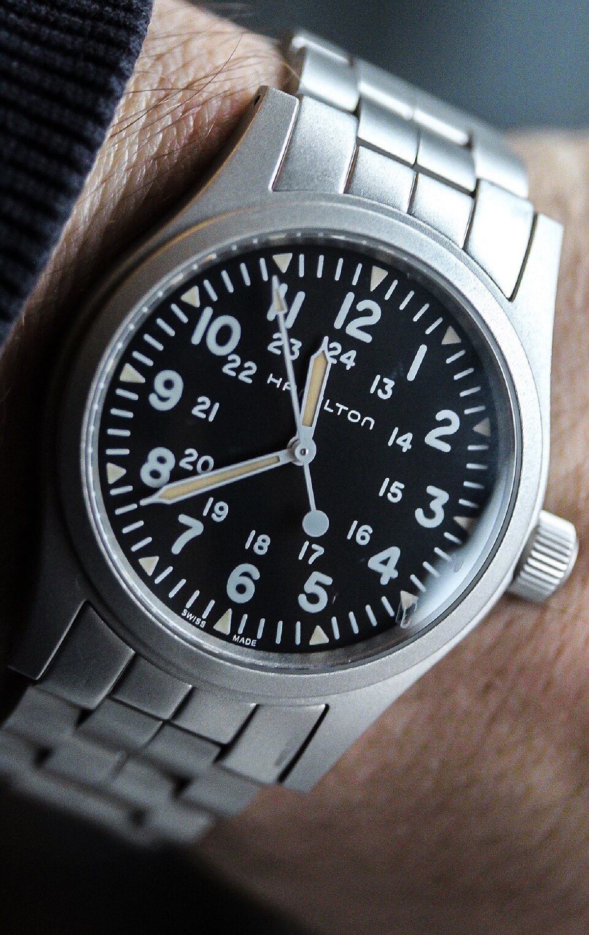 Hamilton Khaki Field Mechanical with black 24-hour military dial, worn on the wrist on a steel bracelet